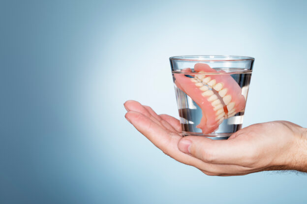 Man holding a glass containing old dentures.